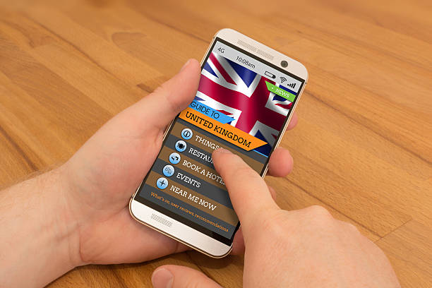 Holding a smartphone in one hand, swiping or using gesture control with the other hand. On the screen is a UK Travel Guide screen.